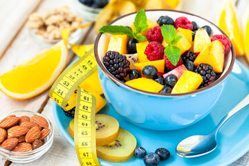 Concept of low calories delicious desserts. Summer fresh bowl with colorful fruit salad. Healthy natural organic food. Tasty sweet snack, light simple tasty lunch. Close up  wooden background
