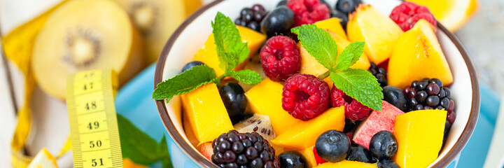 Concept of low calories delicious desserts. Summer fresh bowl with colorful fruit salad. Healthy natural organic food. Tasty sweet snack, light simple tasty lunch. Close up  wooden background banner