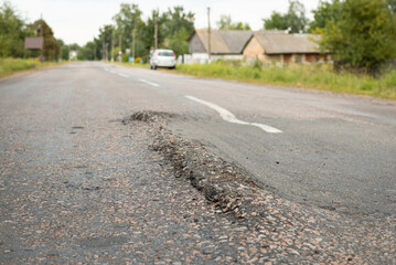 Village with destroyed asphalt road. Humps and holes on the road because of ignoring weight limit