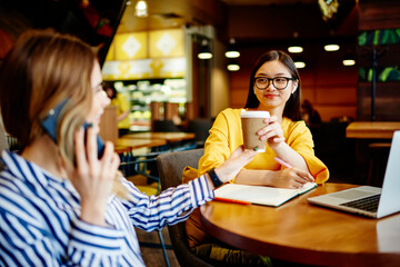 Cheerful young female student doing homework in cafe