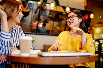 Multiracial ladies talking in cafe near notepad and computer