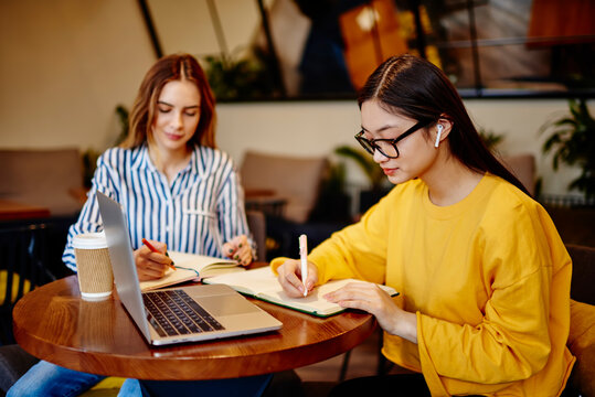 Female students preparing for exam with computer in cafe