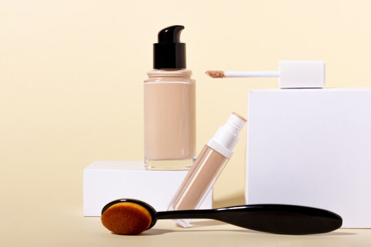 Liquid foundation in a bottle on a stand, makeup brush and concealer. Face corrector on beige background with copy space. Packaging mockup with copy space