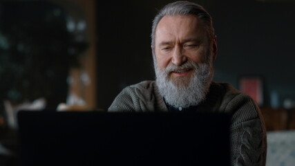 Bearded old man having video call computer indoors. Senior businessman using pc.