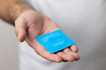 The young man showing the condom into camera. Campaign for safe sex and contraception. Close up male hand holding the condom.