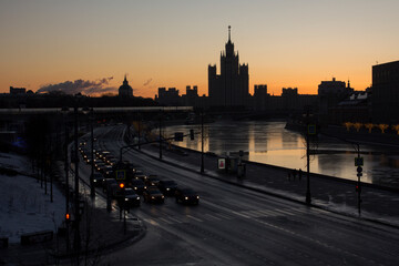 Morning winter urban landscape. Silhouette of Stalin's high-rise on Kotelnicheskaya embankment at sunrise. Morning traffic in Moskvoretskaya Embankment. Moscow, Russia.