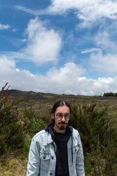 1 hombre serio con pelo largo mirando a la c&aacute;mara con naturaleza a sus espaldas 