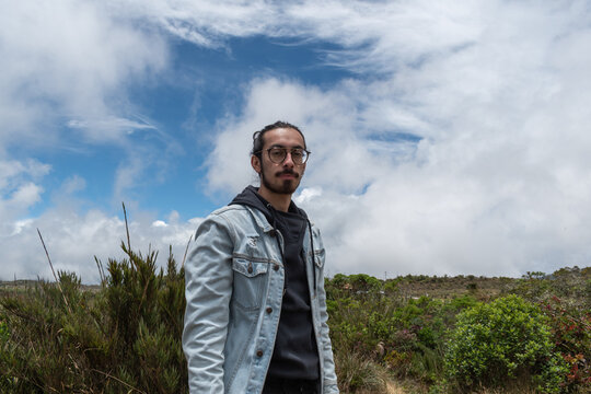 hombre latino con pelo largo mirando a la c&aacute;mara con naturaleza a sus espaldas 
