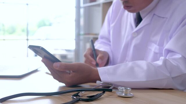 Doctor in uniform using smartphone and writing a short note for making doctor order after examining in clinic. 4K	