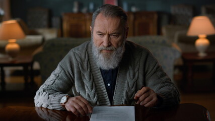 Fototapeta premium Pensive elderly gentleman doing paperwork home. Senior man signing document.