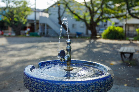 朝の住宅街にある公園の水飲み水栓から出る水と小さな水しぶき