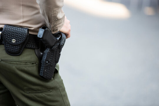 A uniformed Caucasian hand rests on a holstered firearm. 