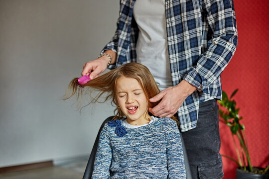 Father Combing, Brushing His Daughter's Hair At Home, Child Making Faces About Hair Pulling