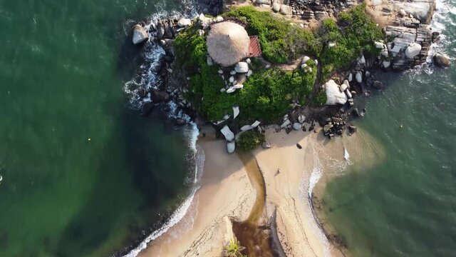 Aerial and top view of a beach, a hut, palm tree and a rock in the middle of the Caribbean Sea in Tayrona National Natural Park, cabo san juan del guia Colombia, South America from a drone