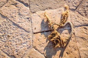 Aufsicht auf ein altes Tau dass in Form eines Herzes auf dem Steinboden des Hafens liegt