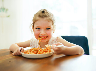 hungry little girl eating spaghetti at home kitchen