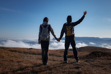 Hiking adventure healthy outdoors people standing talking. Couple enjoying view above clouds on trek. young woman and man in nature wearing hiking backpacks and sticks.