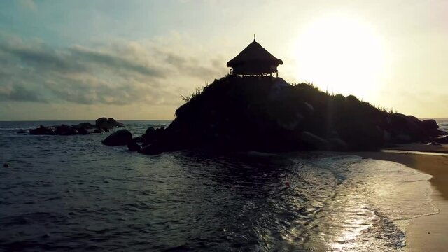 Aerial view sunset of a beach and a cabin in the middle of the Caribbean Sea in Tayrona National Natural Park, Colombia, South America by a drone