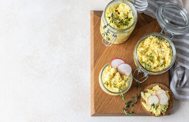 Tartlets with egg pate or salad and radish and thyme on light stone background. Egg dip in glass jar. Top view. Copy space.