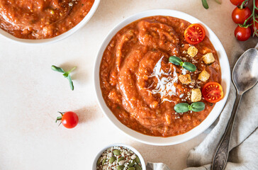 Vegetable soup with baked tomato, bell pepper, cream, breadcrumbs and micro greens in white bowl on light concrete background. Top view.