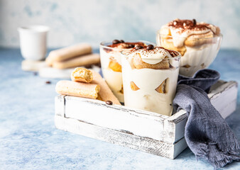Traditional Italian dessert tiramisu in glass, light stone background. Coffee flavored portion dessert made of ladyfingers and mascarpone decorated with cocoa.
