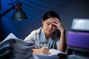 Asian woman writing documents in overtime at night.Working deadline in office.