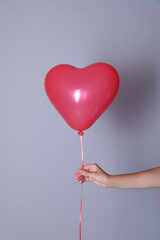 Woman holding heart shaped balloon on light background, closeup