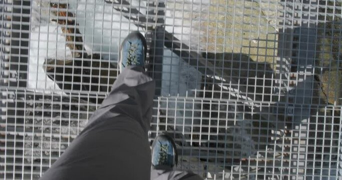 Point of view of man legs in hiking pants walking on steel bridge over a water stream in High Tatra mountains, Slovakia. Adventure.