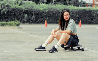 Portrait beautiful sportive Asian female skater wearing hipster shirt with shorts, smiling with happiness, sitting and posing with skateboard outdoor with copy space. Activity and Adventure Concept.