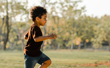 Portrait of Caucasian little white curly hair boy, running and playing with happiness and running in park at evening summer time with warm light. Education Concept.