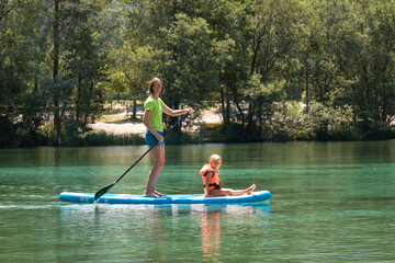 Young smiling woman paddling on a SUP - stand up paddle board, while her daughter sitting on it