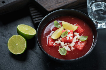 Bowl of gazpacho cold soup made of watermelon, horizontal shot on a black stone background