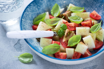 Closeup of salad with melon, red tomatoes and fresh green basil served in a blue bowl, selective focus, studio shot