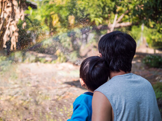 Fototapeta premium Authentic asian child boy and father making beautiful rainbow by water splash, sunlight together in garden. Concept of learning nature, fun family activity, good relationship.