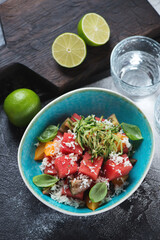 Turquoise bowl with watermelon, tomatoes, bryndza and cucumber salad, vertical shot on a dark grey stone background, elevated view