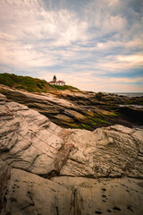 Fototapeta na wymiar Dramatic cloudscape over the rugged rock beds with the view of Beavertail State Park Lighthouse