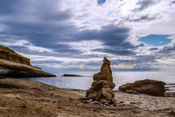 Beach surrounded by mountains with stone column. Storm concept..
