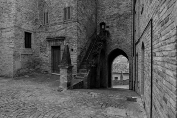 Fototapeta na wymiar Glimpse of a small medieval village in the province of Fermo, in the background the Marche countryside, very cloudy sky, black and white photo.