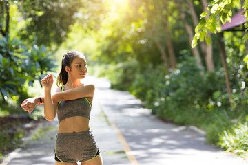 Pretty girl warms up her body before jogging outdoors in the park.