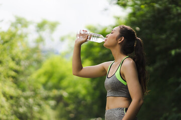 A thirsty Asian female athlete is drinking water after a workout.