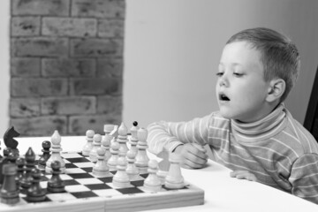 Cute seven year old child boy playing chess at home on a white wooden table. Selective focus. Close-up. Portrait