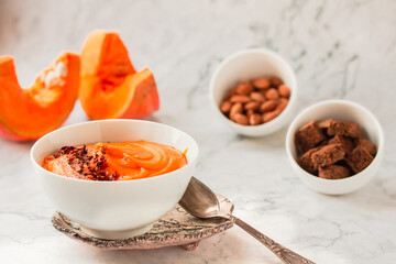 Pumpkin soup and organic pumpkins on marble table. Seasonal autumn food - Spicy pumpkin and carrot soup