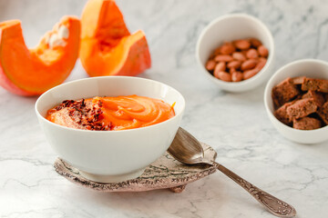 Pumpkin soup and organic pumpkins on marble table. Seasonal autumn food - Spicy pumpkin and carrot soup