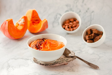 Bowl of tasty pumpkin soup ith chili flakes pepper, nuts and croutons.Space for text on marble table