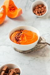Pumpkin soup and organic pumpkins on marble table. Seasonal autumn food - Spicy pumpkin and carrot soup