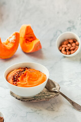 Tasty appetizing pumpkin creamy soup decorated with chili flakes pepper served in white bowl on marble background. Selective focus