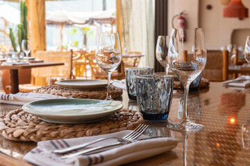 Mesa de restaurante turístico en la playa con copas, vasos, platos y cubertería completa
