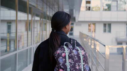 Back view of afro-american schoolgirl with backpack walk outdoors