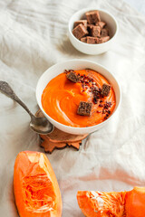 Pumpkin and carrot soup with chili flakes pepper on a on autumn comfort background. Copy space