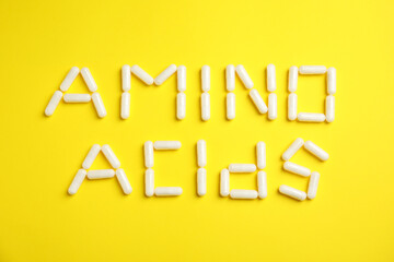 Phrase Amino acids made of pills on yellow background, flat lay